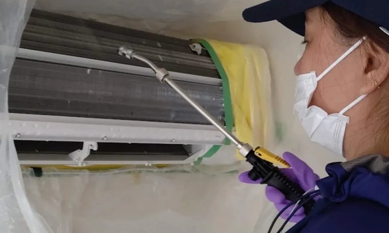 高圧洗浄機でエアコン内部を洗浄するスタッフ